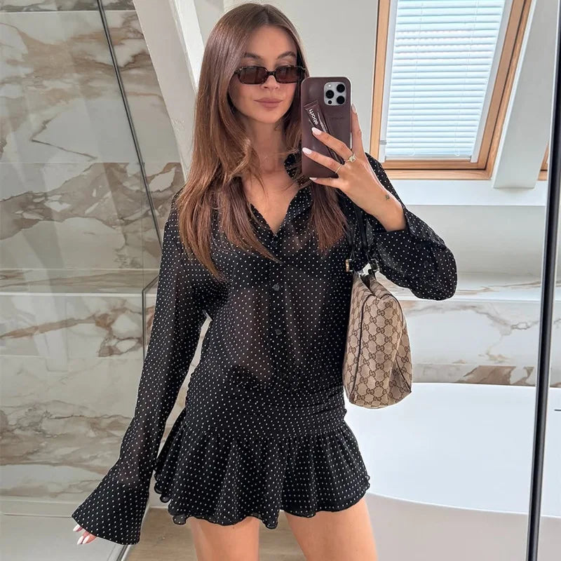 Woman taking a mirror selfie wearing a black polka dot dress in a bathroom.