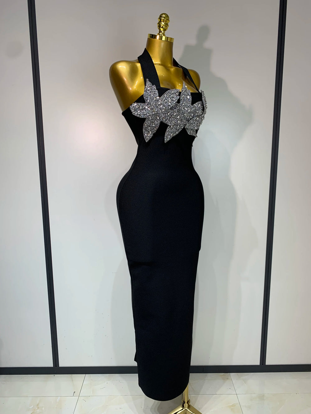 Black evening gown with silver floral embellishments on a mannequin against a white wall.