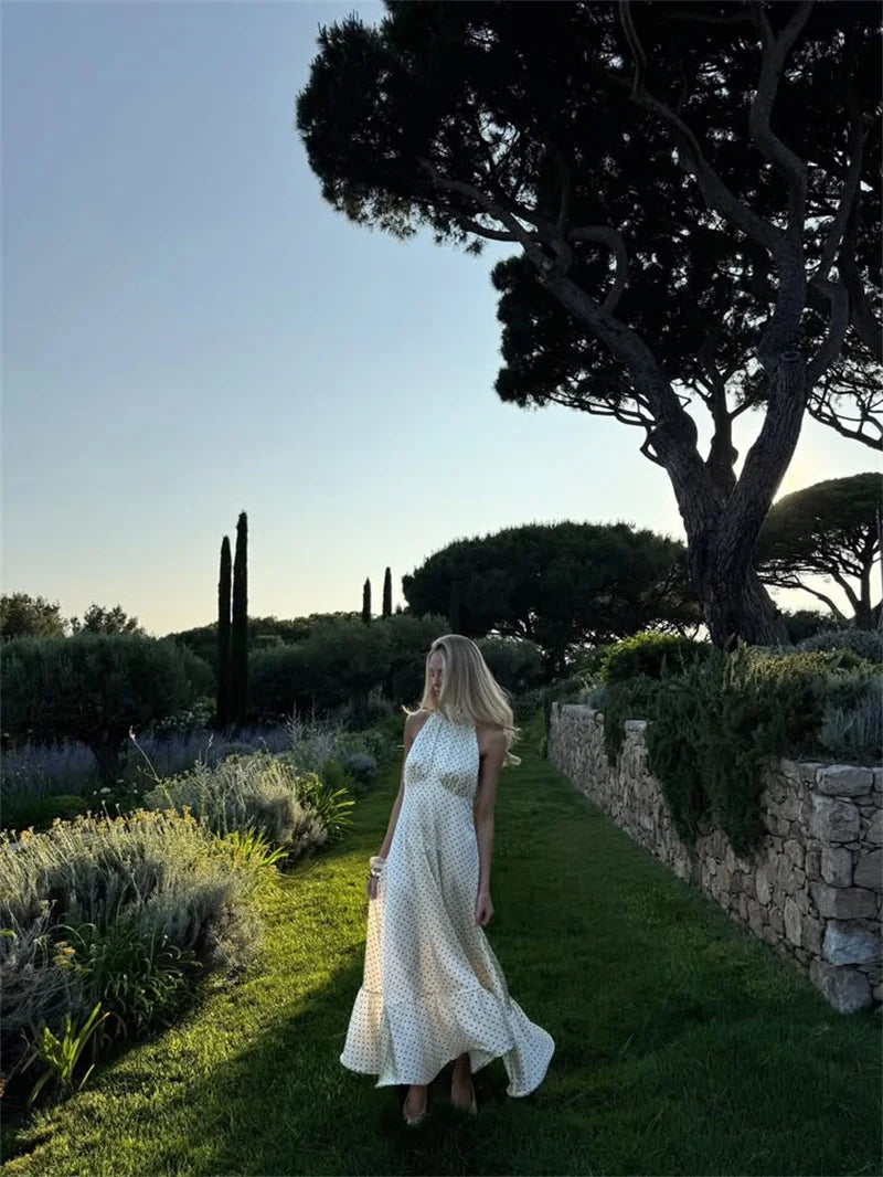 Woman in a white dress standing in a garden with trees and lavender plants.