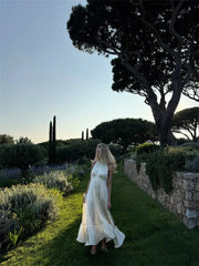 Woman in a white dress standing in a garden with trees and lavender plants.