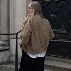 Person wearing a beige jacket standing in front of a large black door.