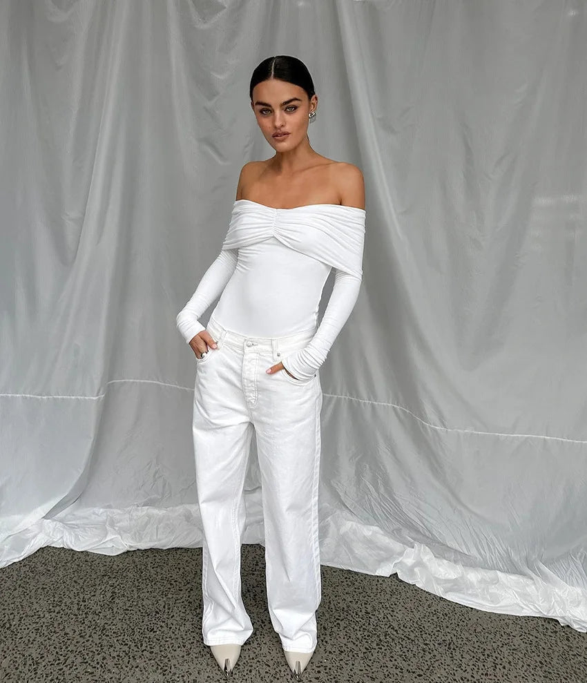 Person wearing a white off-shoulder top and pants against a gray curtain background