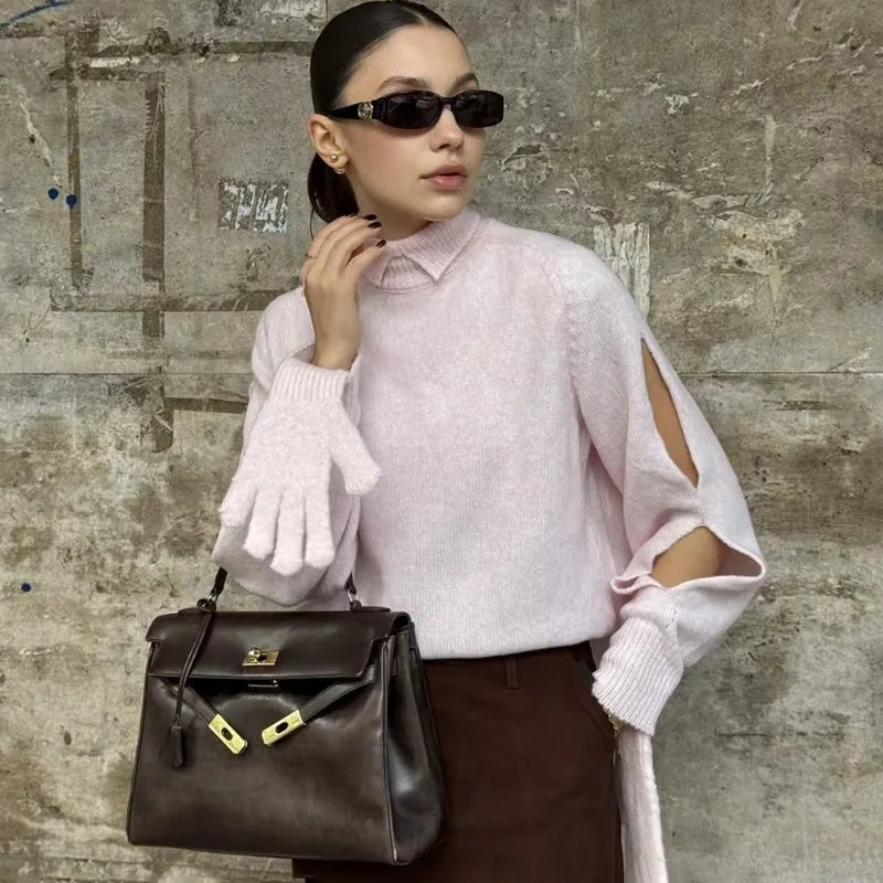 Woman holding a brown leather handbag against a textured wall.