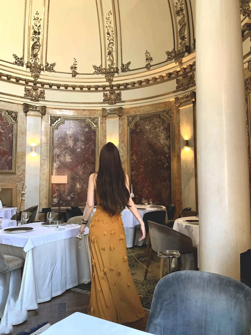 Woman in a yellow dress standing in an elegant restaurant with ornate decor.