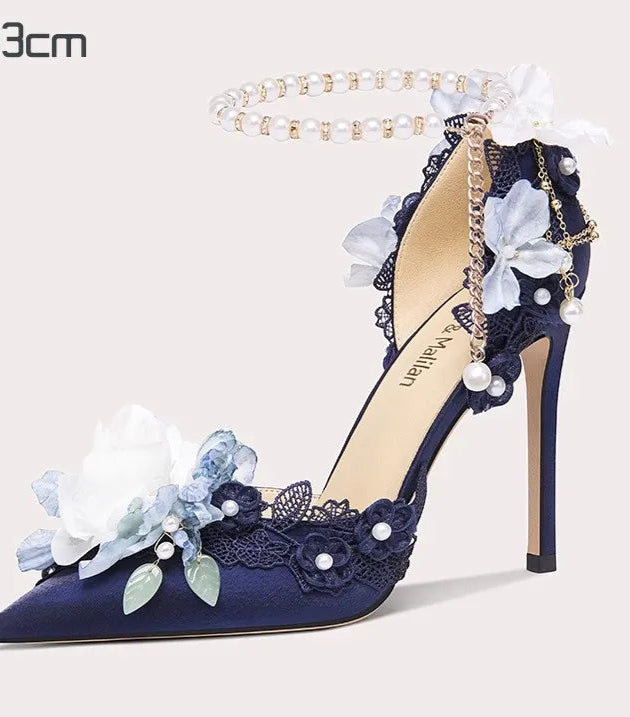 Navy blue high-heeled shoe with floral and pearl details on a light gray background