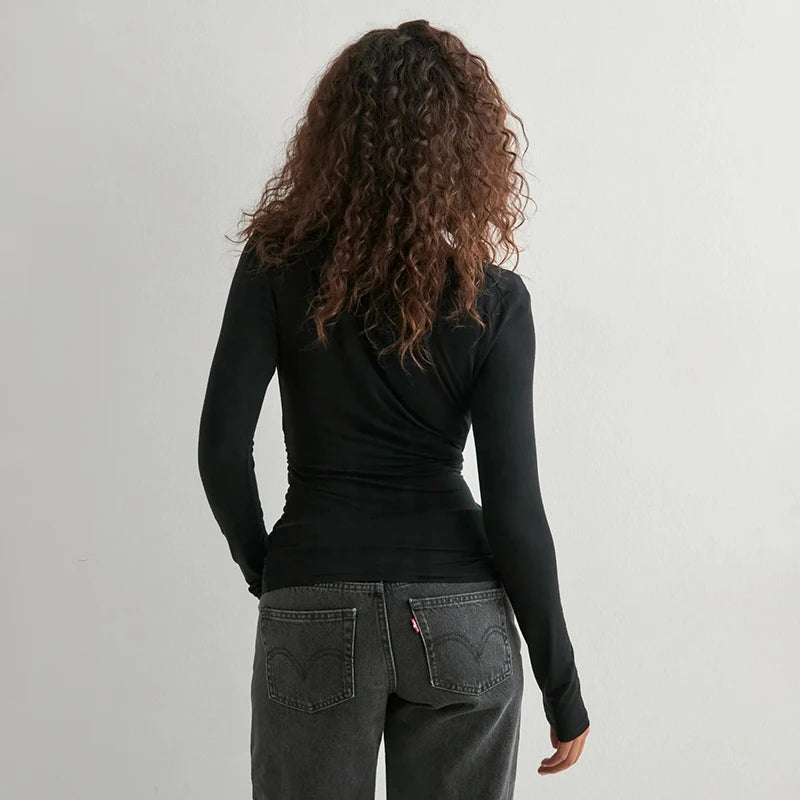 Person wearing a black long-sleeve top and gray jeans on a plain background