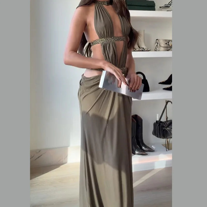 Woman in a long olive green dress holding a clutch in an indoor setting with shelves in the background.