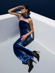 Woman in a blue velvet outfit sitting on a white ledge with a blue background