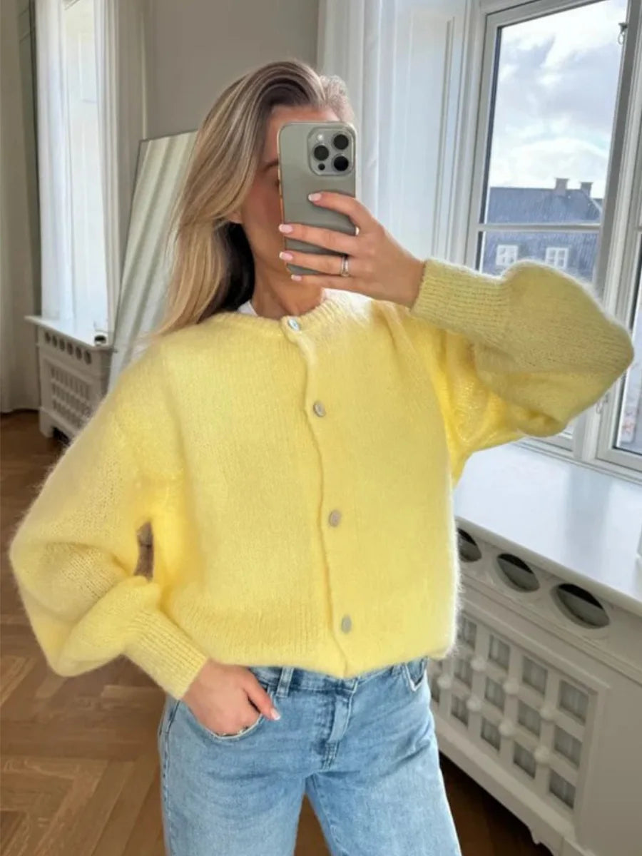 Person wearing a yellow cardigan and blue jeans taking a mirror selfie.