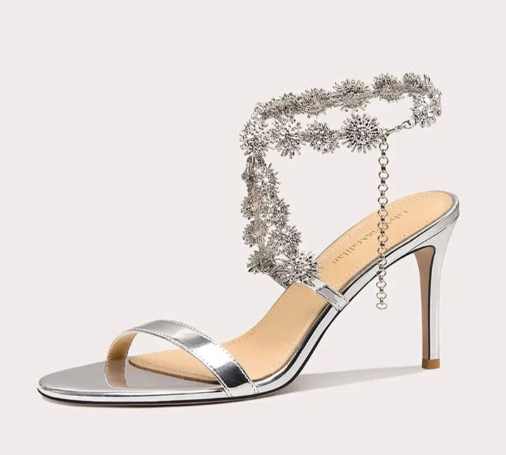 Silver high-heeled sandal with decorative chain on a white background