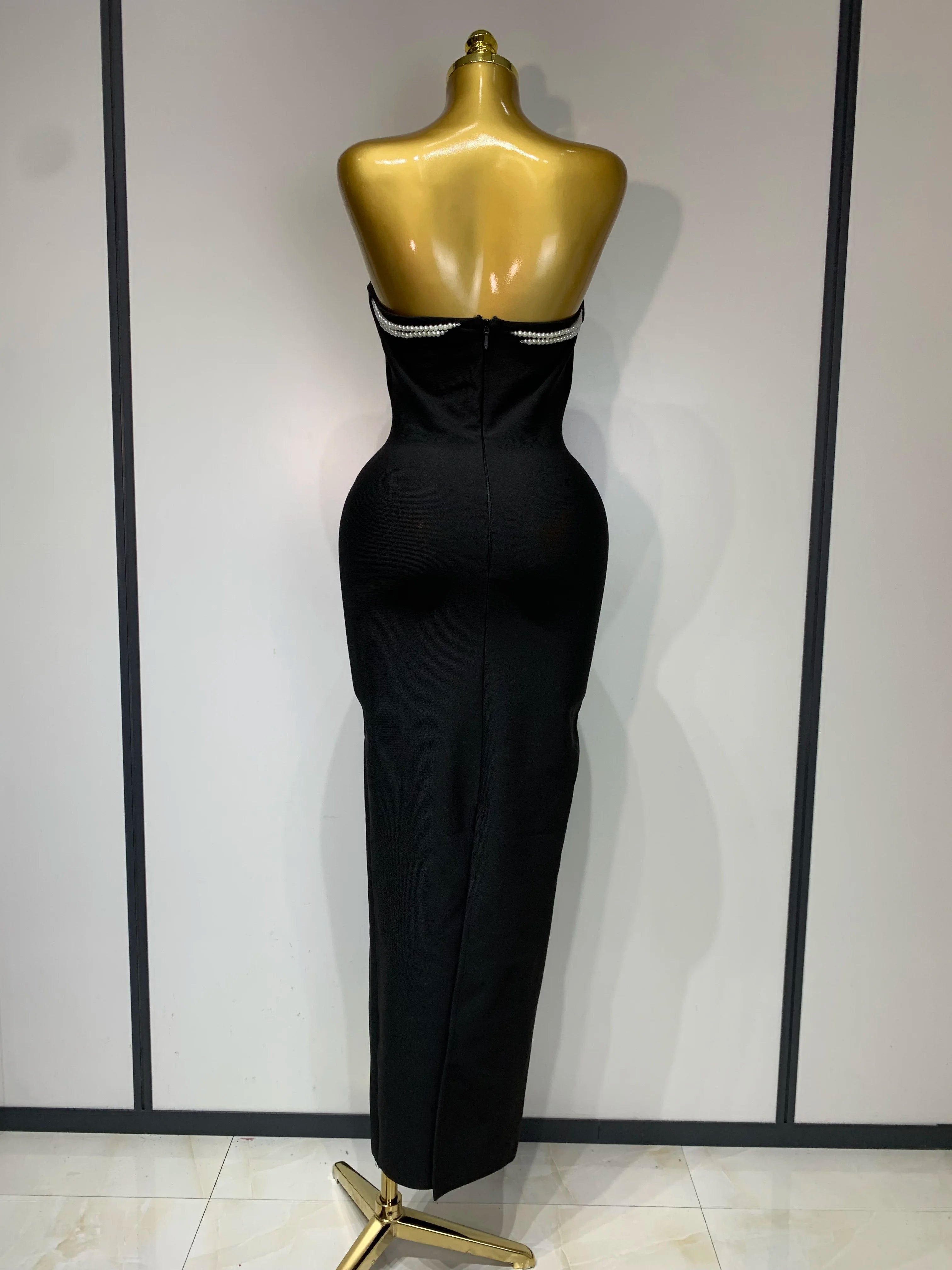 Black evening gown on a gold mannequin against a white background
