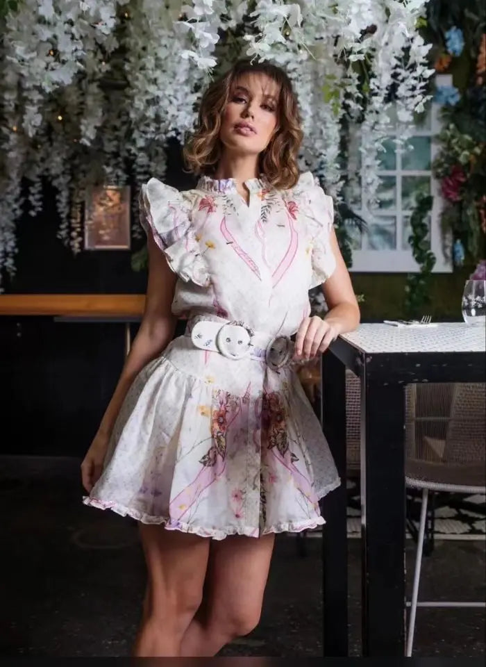 Woman wearing a floral dress with a white belt in an indoor setting with plants.