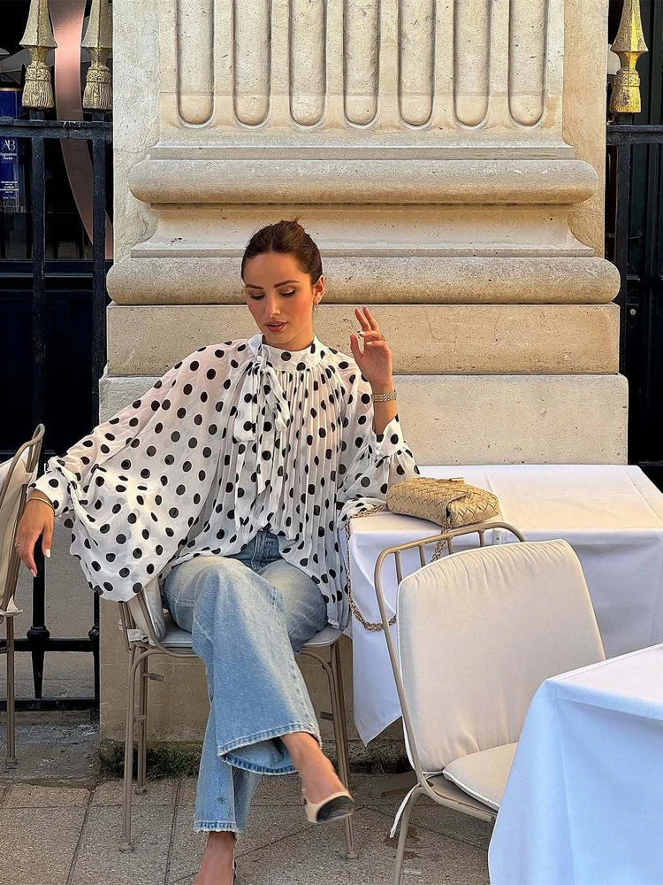 Woman sitting at an outdoor cafe table in a polka dot blouse and jeans.