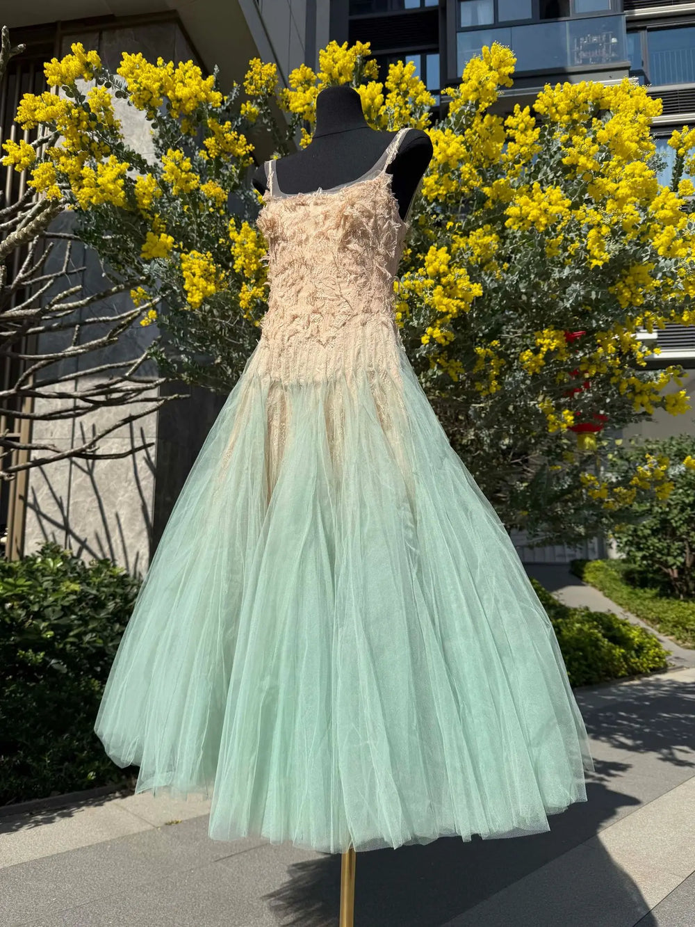 Mannequin wearing a dress with a floral top and light green skirt in front of yellow flowers.