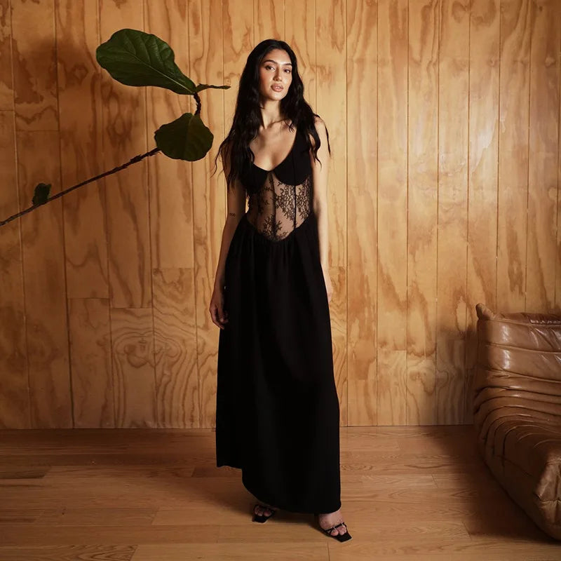 Woman in a black dress standing against a wooden wall with a plant.