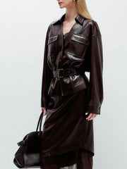 Person wearing a dark brown leather outfit with a belt and carrying a matching bag on a light gray background