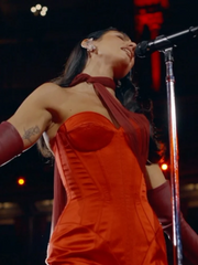 Person in a red dress singing into a microphone on stage at night.