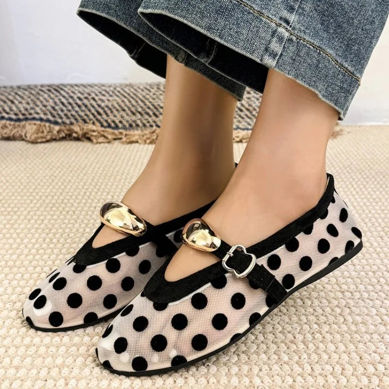 Pair of polka dot mesh ballet flats with buckle straps on a textured surface.