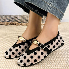 Pair of polka dot mesh ballet flats with buckle straps on a textured surface.