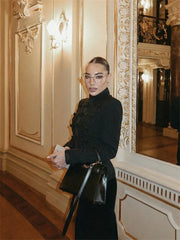 Woman in a black coat standing in an ornate interior setting