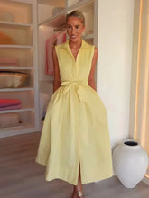 Woman wearing a yellow dress in a room with shelves and a vase.