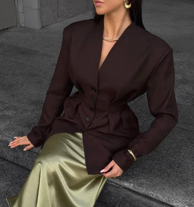 Woman wearing a brown blazer and green skirt sitting on a stone step.