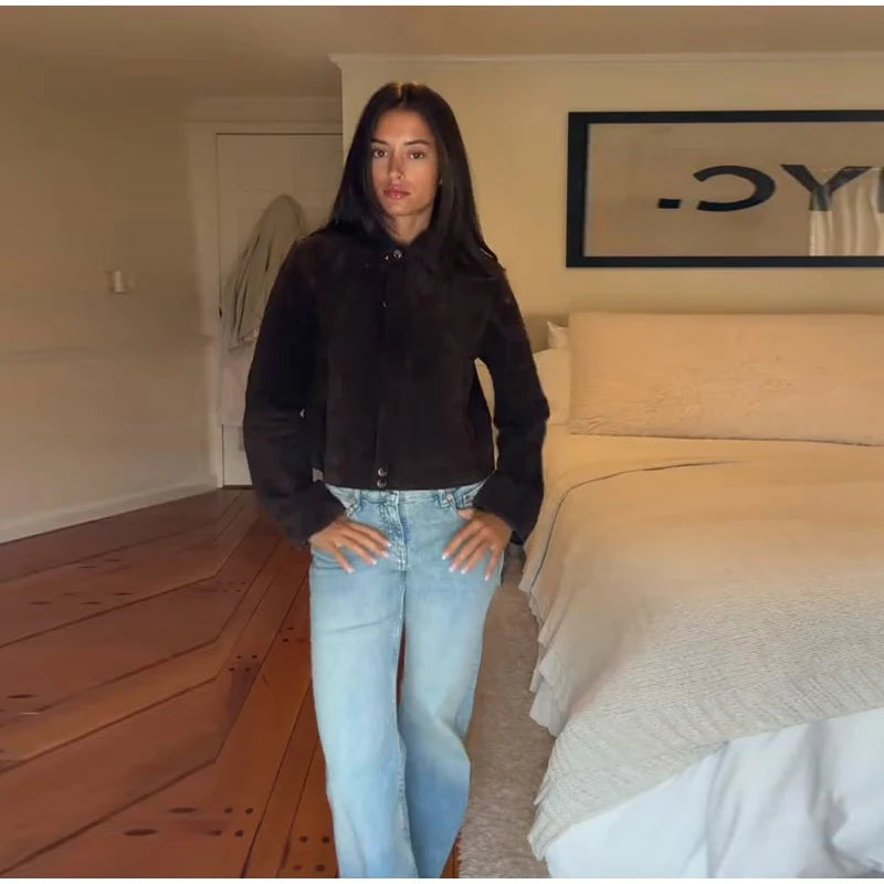 Person wearing a black jacket and light blue jeans standing in a bedroom.