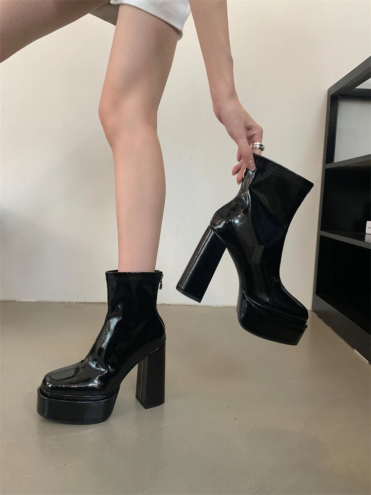 Person wearing black platform boots holding one boot up, on a neutral background