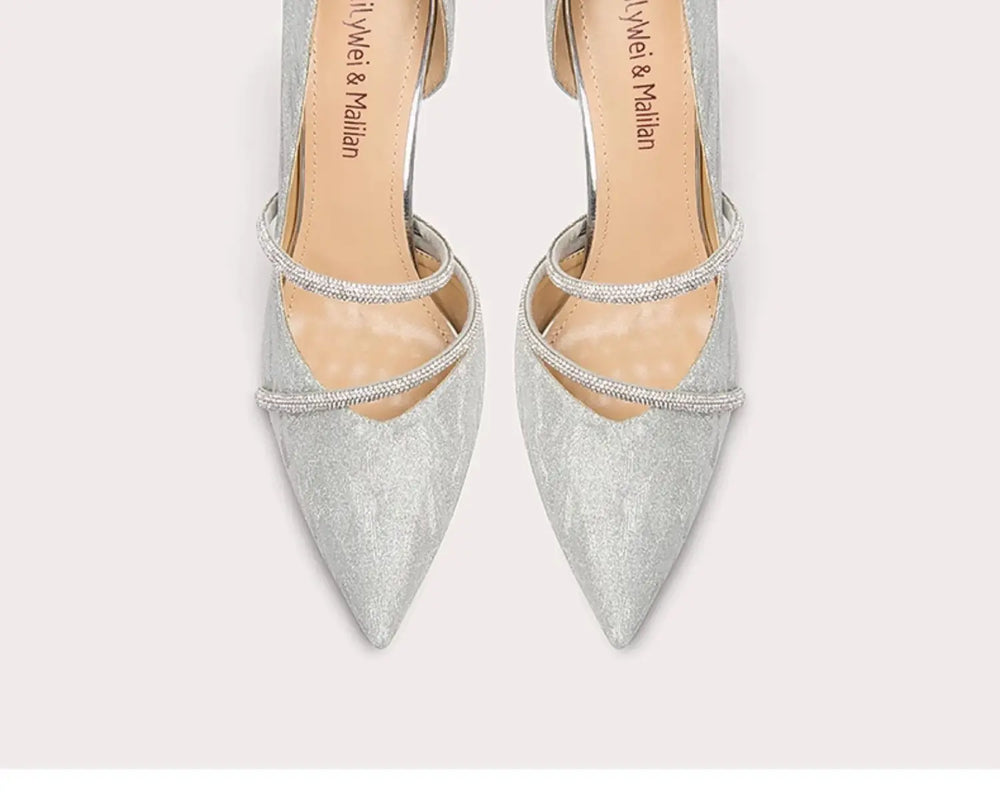 Pair of silver pointed-toe high heels with thin straps on a light gray background