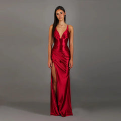 Woman wearing a red satin gown with a deep neckline and high slit on a gray background