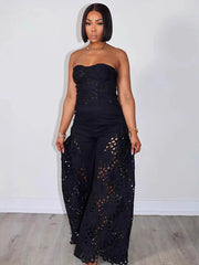 Woman wearing a black strapless top and wide-leg pants with cut-out details against a white wall.