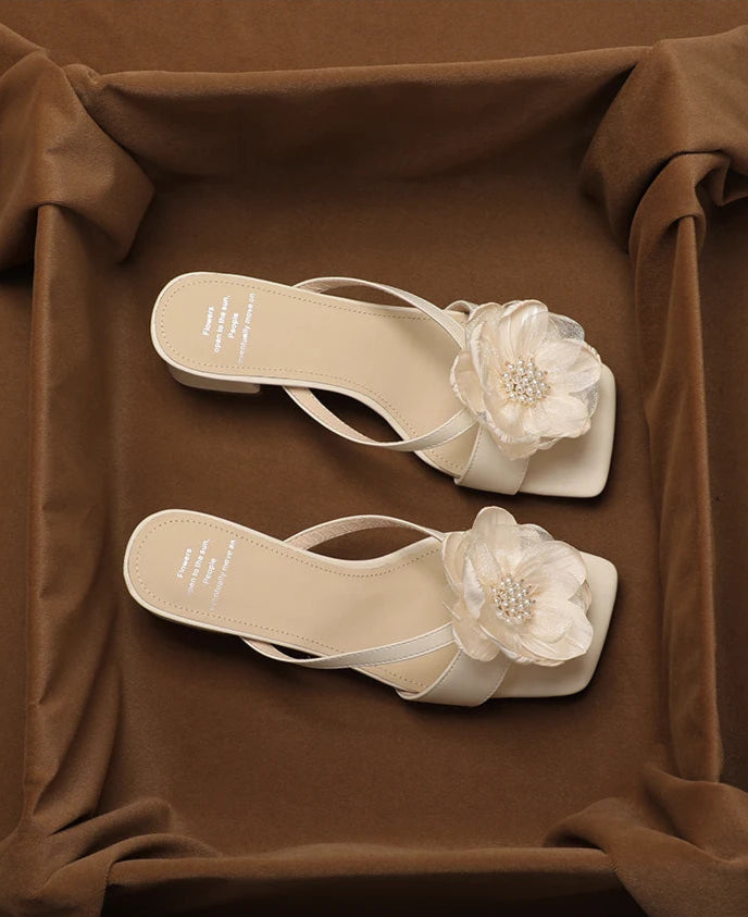 White sandals with floral decorations on a brown fabric background
