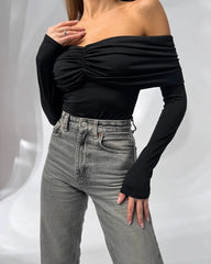 Person wearing a black off-shoulder top and gray jeans on a white background