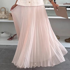 Person wearing a light pink pleated skirt with a blurred background of shoes and bags.