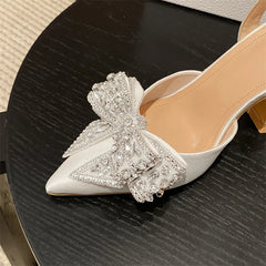 White high-heeled shoe with a large decorative bow on a dark surface