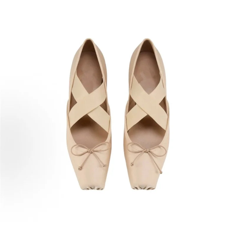 Pair of beige ballet shoes with straps on a white background