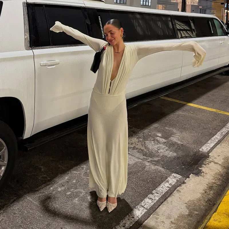 Woman in a long, light-colored dress standing in front of a white limousine.