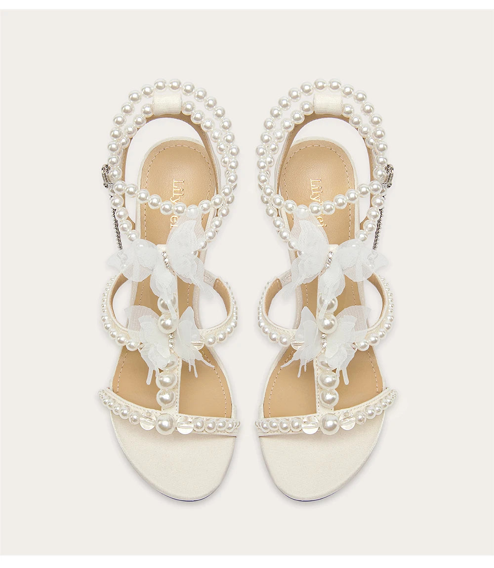 White sandals with butterfly and pearl details on a light gray background