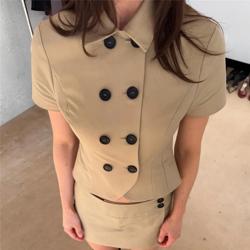 Person wearing a beige suit with black buttons in an indoor setting