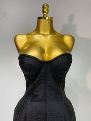 Black strapless dress on a gold mannequin against a gray background