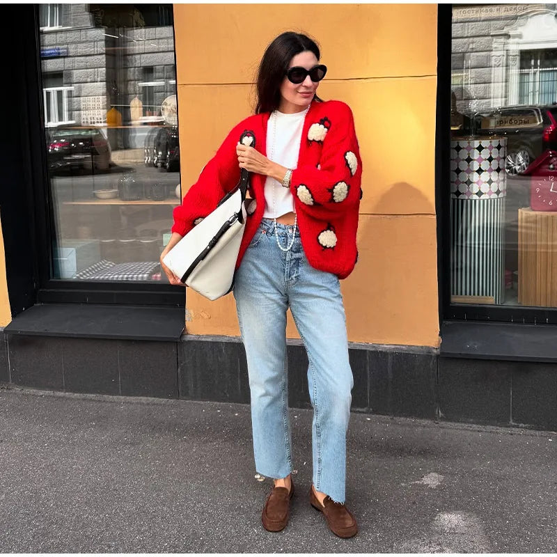 Woman wearing a red jacket with white polka dots, light blue jeans, and brown shoes, standing against a yellow wall.