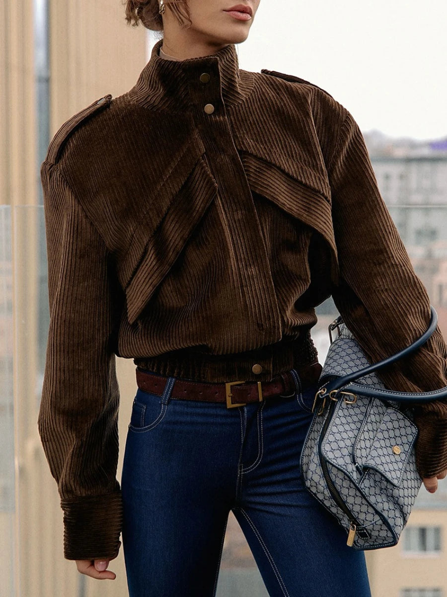 Person wearing a brown corduroy jacket and blue jeans, holding a patterned handbag.