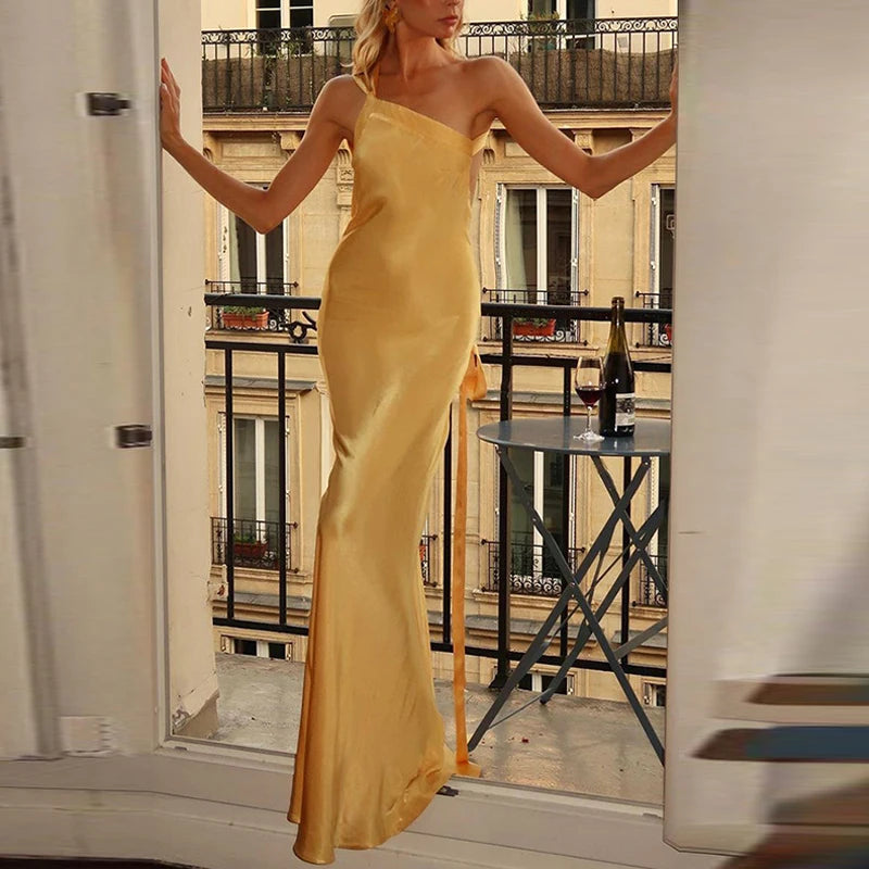 Woman in a yellow dress standing on a balcony with a bottle of wine.