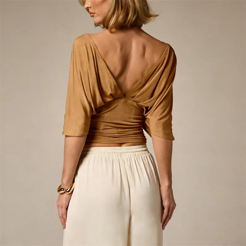 Woman wearing a mustard yellow top with a back design and white pants on a beige background
