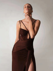 Woman wearing a brown dress with a deep neckline and slit on a plain background