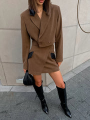 Person wearing a brown suit with black accents and black knee-high boots against a light-colored wall.