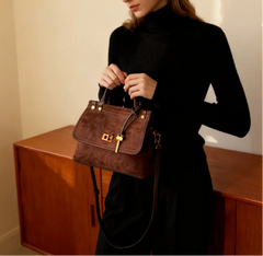 Woman holding a brown handbag in front of a wooden cabinet