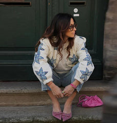 Woman sitting on steps wearing a floral-patterned sweater with a pink handbag beside her.