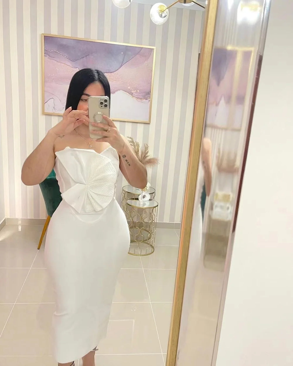 Person wearing a white strapless dress with a bow detail, standing in front of a mirror.