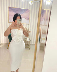 Person wearing a white strapless dress with a bow detail, standing in front of a mirror.